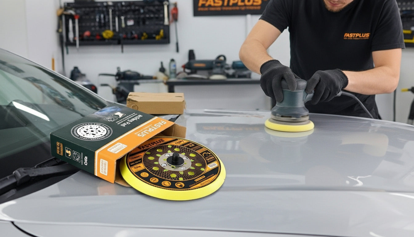 Person using a car polisher on a car hood with a box of fastplus backing pad in a workshop setting.